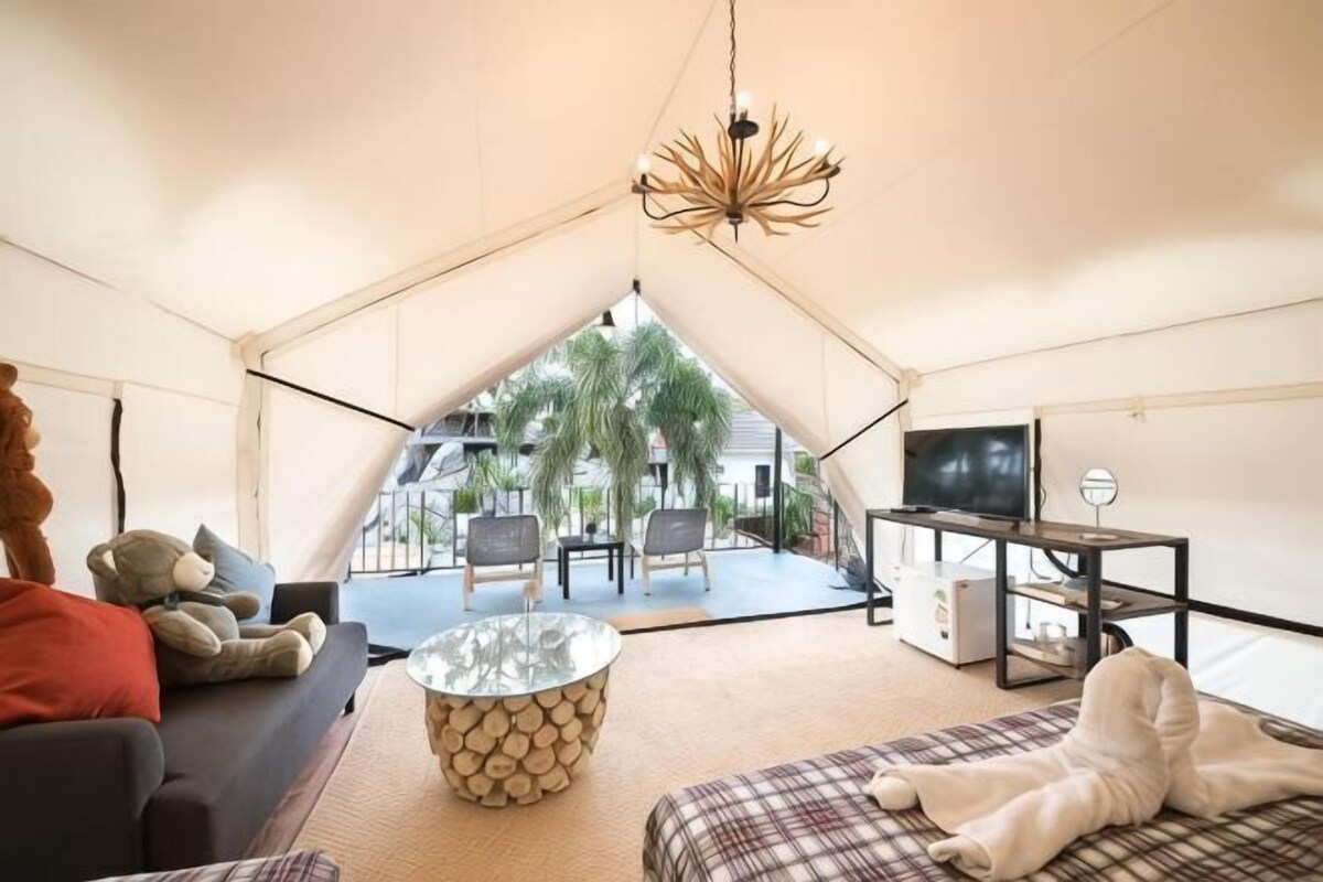 A tented accommodation with a sofa, a coffee table, a TV, and a view of the outdoors.