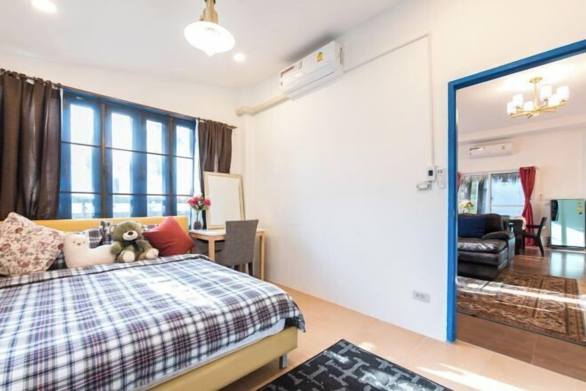 Un dormitorio con cama, escritorio y silla. Hay una ventana con cortinas, un equipo de aire acondicionado y un espejo.