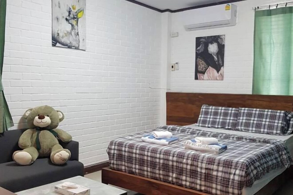 Una habitación con una cama, una silla y un gran osito de peluche.