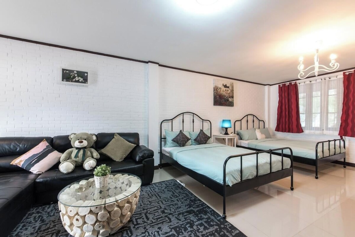 Ein Zimmer mit einer schwarzen Ledersofa, einem Glastisch, einem Metallbettgestell, einem Nachttisch mit Lampe und einem Fenster mit roten Vorhängen.