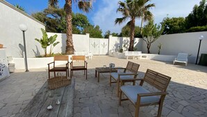 Un patio al aire libre con mobiliario de madera, suelo de piedra y palmeras.