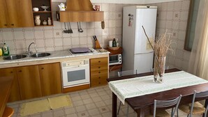 Una cocina compacta con fregadero, estufa, horno y microondas. Hay una mesa de comedor con sillas y un florero con ramas.