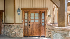 A wooden double door with a stone base, a stone wall with a number plaque, and a wooden beam structure above.