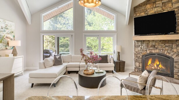 A modern living room with a stone fireplace, large windows, and a flat-screen TV.