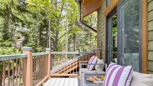 A wooden deck with a sofa and table, surrounded by trees.