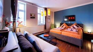 Una camera d'albergo moderna con un divano, un letto con lenzuola arancioni, una TV a schermo piatto e una finestra con tende.