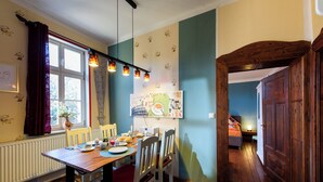 Zona pranzo con tavolo in legno, sedie, finestra con tende, termosifone e parete con un poster.