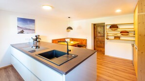 A compact kitchen with a central island, a wooden dining table, and a wooden cabinet with shelves.