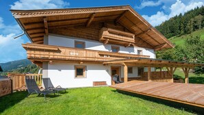 A two-story wooden house with a balcony, a deck, and a view of the surrounding hills.