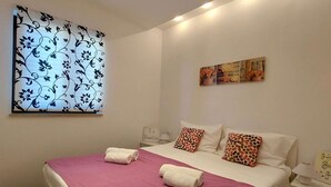 Ein Hotelzimmer mit Bett, Kissen, Nachttisch, Wandbild und Fenster mit Blumenmuster.