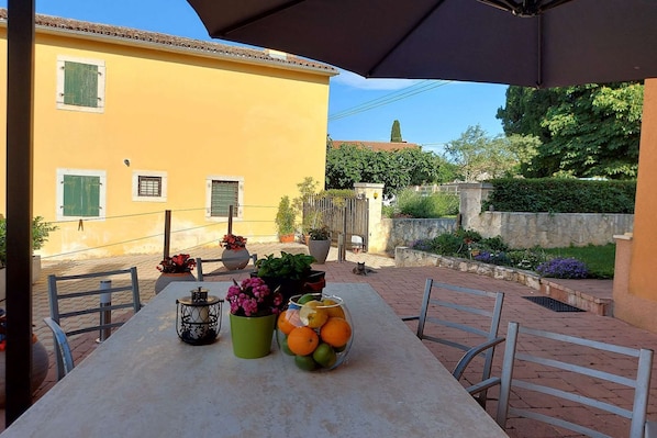 An outdoor patio with a table set for dining, surrounded by potted plants and a stone wall.