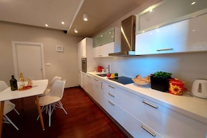 A modern kitchen with white cabinets, a stainless steel range hood, and a dining area with a white table and chairs.