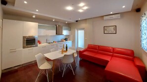 Eine moderne Küche mit weißen Schränken, ein Essbereich mit weißem Tisch und Stühlen sowie ein rotes Sofa im Wohnbereich.
