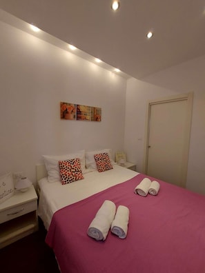 A bedroom with a bed, pillows, a nightstand, a door, and wall art.