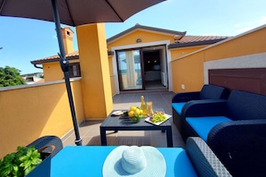 Un balcón con una mesa azul, muebles de mimbre y una planta en maceta.