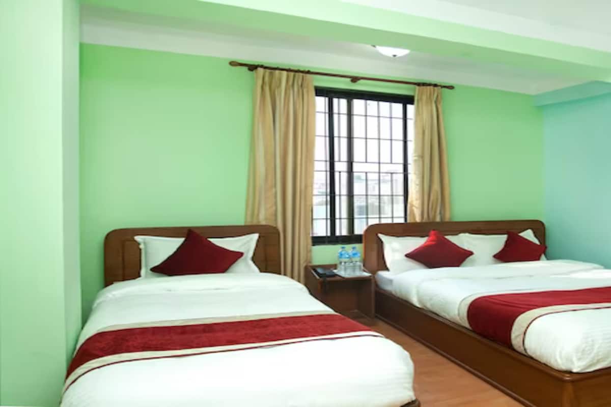 A room with two beds, green walls, a window with curtains, and a nightstand with a water bottle.