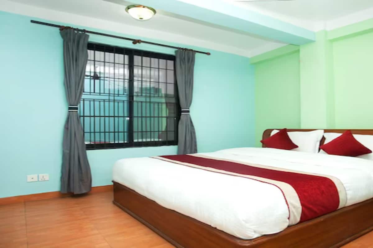 A bedroom with a wooden bed, a nightstand with water bottles, and a window with curtains.
