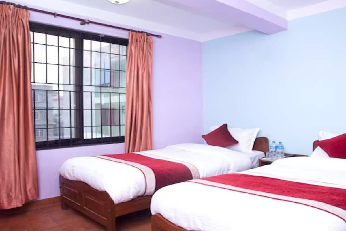 A hotel room with two beds, a window with curtains, and a nightstand with water bottles.