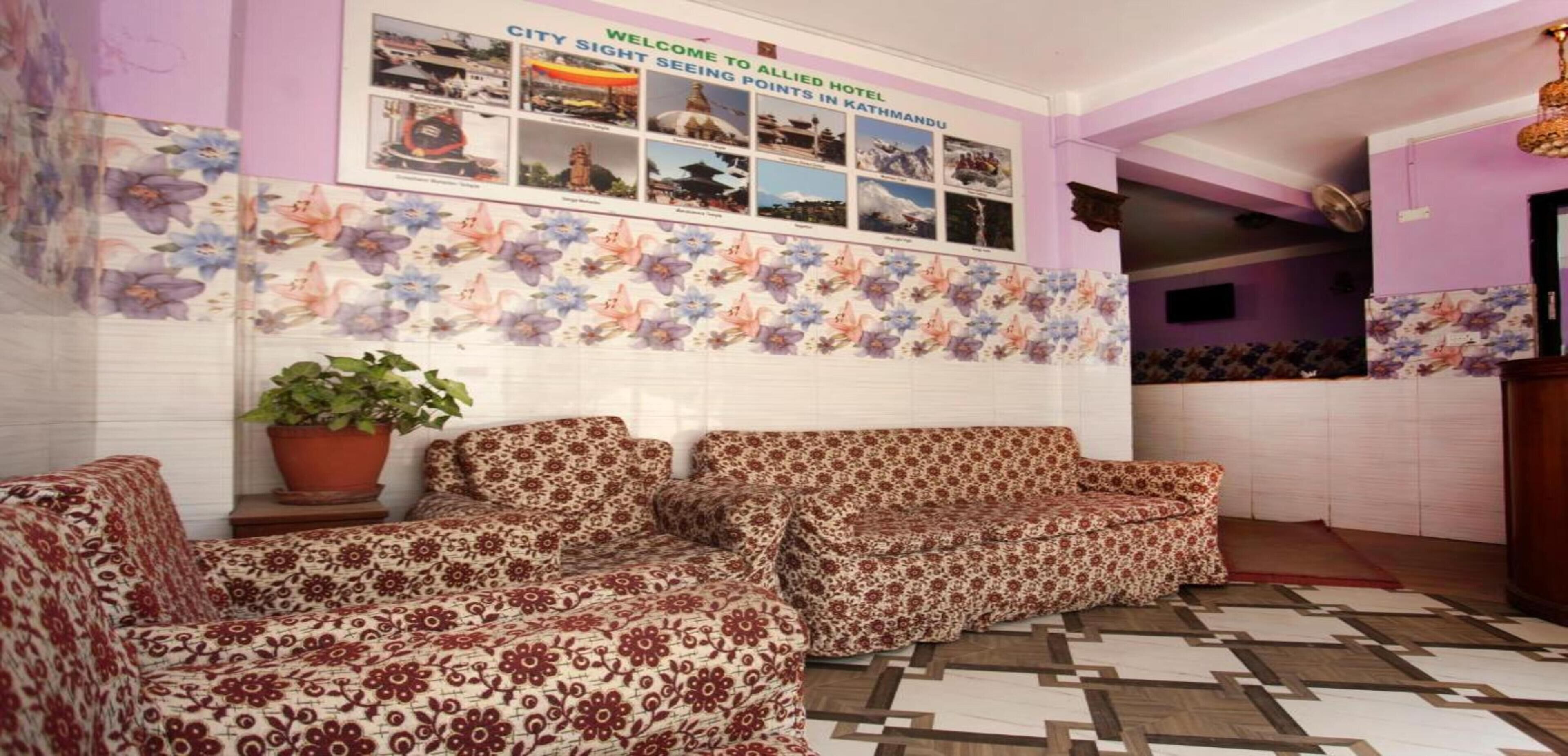 Un hall d’hôtel avec des canapés à motifs floraux, un panneau d’accueil et un mur orné de photos des principaux sites touristiques de la ville.