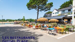 An outdoor seating area with tables and chairs, a large tree, and a building with a sign that reads "ET GLACES". - Grande Villa à 400m de la Plage, Idéale Famille par Groom (Ploemeur)