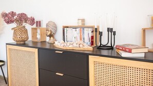 A wooden console table with a woven basket, a vase with dried flowers, a small wooden box, a candle, a book, and a candle holder with multiple candles. - Grande Villa à 400m de la Plage, Idéale Famille par Groom (Ploemeur)