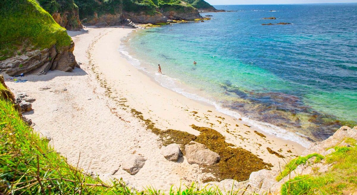 Ein Strand mit klarem türkisblauem Wasser und einer felsigen Küstenlinie.