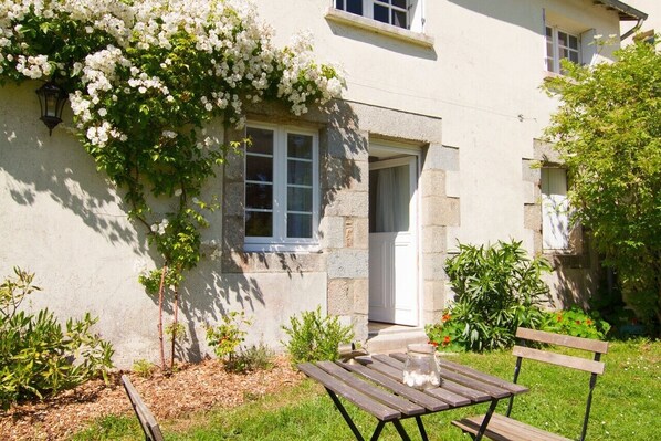 Una casa con jardín, un banco de madera y una puerta blanca.