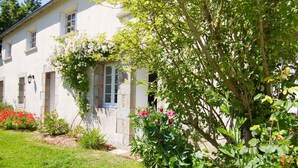 A white building with a garden, a tree, and a flower bed. - Apartment 'Prat Bras - T1 Cocooning' with Shared Garden and Wi-Fi (Clohars-Carnoët)