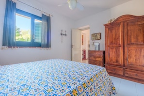 Une chambre à coucher avec un lit, une armoire, une fenêtre avec des rideaux et un ventilateur de plafond.