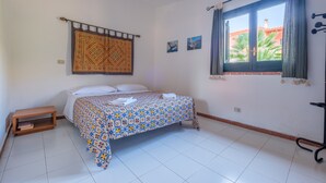 Ein Schlafzimmer mit einem Bett, einem Deckenventilator, einem Fenster mit Vorhängen, einem kleinen Nachttisch und einer Wandteppich.