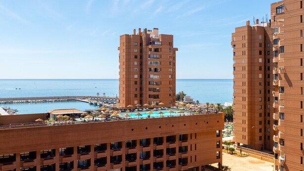 A high-rise hotel with balconies, a pool area, and a view of the sea.