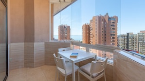 A balcony with a white table and chairs, a book on the table, and a view of tall buildings and the sea.