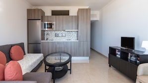 A compact living space with a kitchenette, a sofa, a small table, a TV, and a bookshelf.