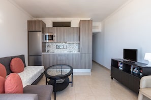 A compact living space with a kitchenette, a sofa, a small table, a TV, and a bookshelf.