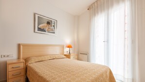 Ein Schlafzimmer mit einem Bett, einem Nachttisch, einer Lampe, einem Bild an der Wand und einem Fenster mit Vorhängen.