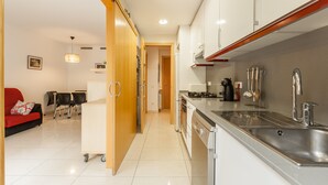 Eine moderne Küche mit Edelstahlgeräten, ein Essbereich mit einem roten Sofa und ein Flur, der zum Wohnzimmer führt.