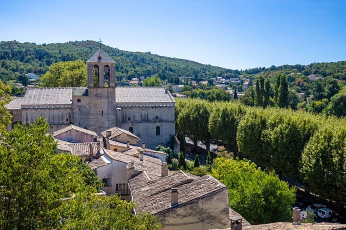 A historic building with a bell tower, surrounded by trees and a hilly landscape.