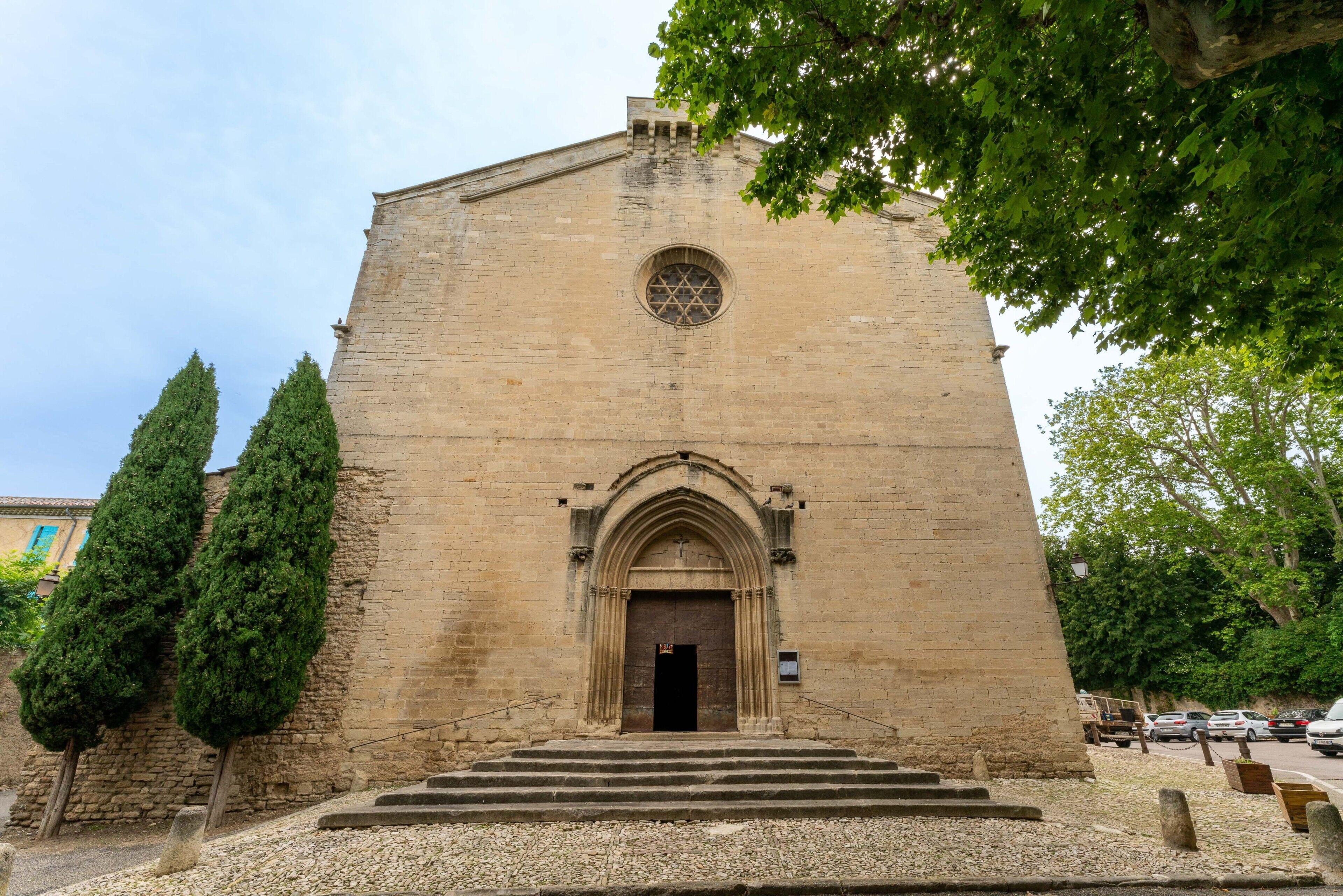 A historic building with a large arched entrance, steps leading up to it, and a circular window above the door.
