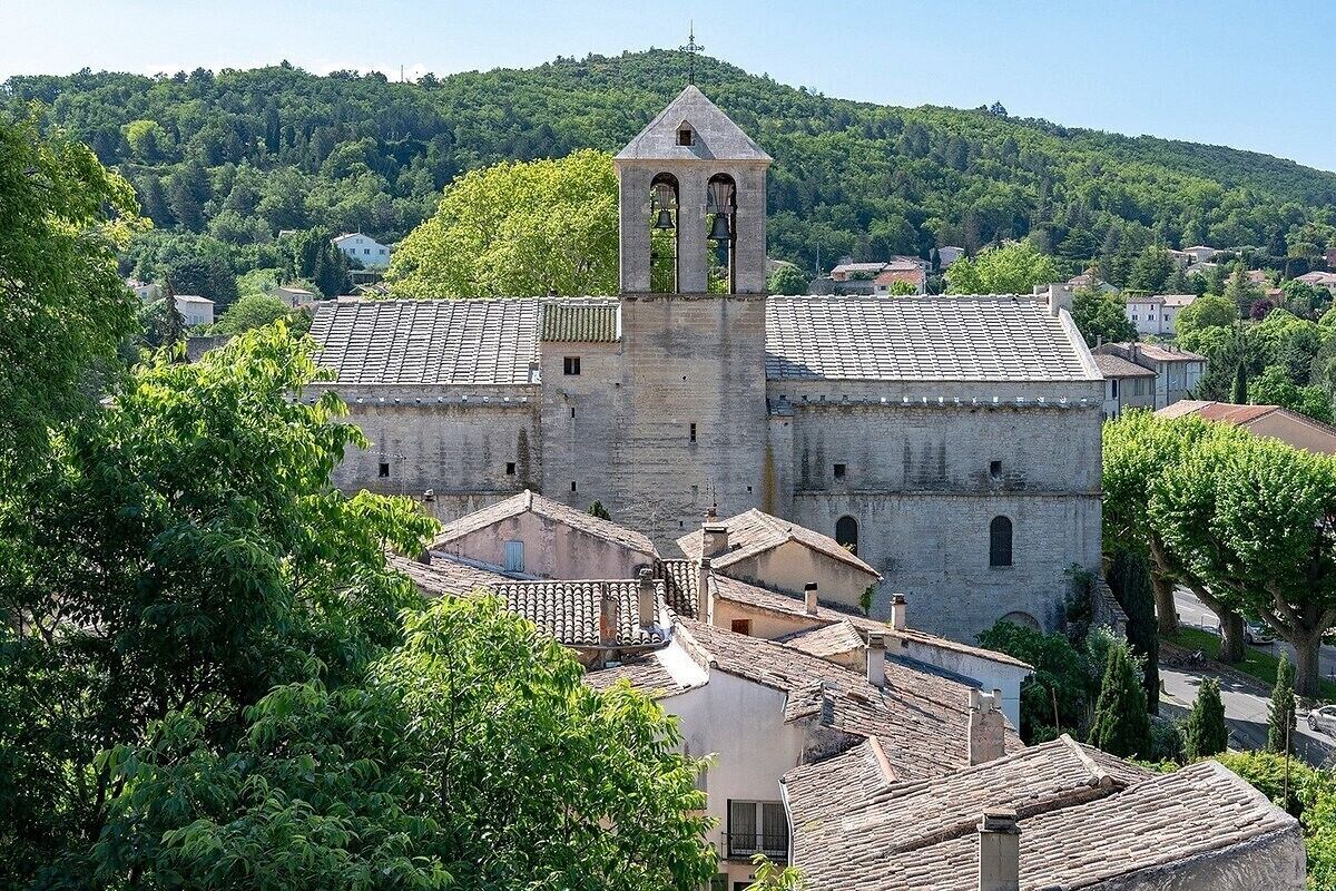 A historic stone building with a bell tower, surrounded by trees and residential buildings.