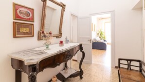 Una habitación con una consola de mesa con cubierta de mármol, un espejo grande, cuadros enmarcados y una puerta que da a otra habitación.