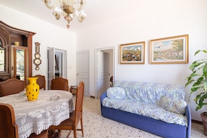 Un coin repas comprenant une table, des chaises, un vase jaune, un canapé bleu et deux tableaux encadrés accrochés au mur.