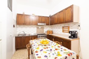 A compact kitchen with wooden cabinets, a gas stove, a sink, and a table with a fruit-patterned tablecloth.