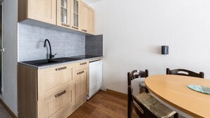 A compact kitchen with wooden cabinets, a dishwasher, a black faucet, and a round wooden table with chairs.
