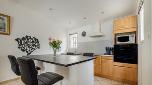 A kitchen with a central island, black chairs, wooden cabinets, a microwave, and a clock on the wall. - Holiday Home 'Maison Piscine Chauffe Jacuzzi' with Private Terrace, Private Garden and Wi-Fi (Tourrettes)