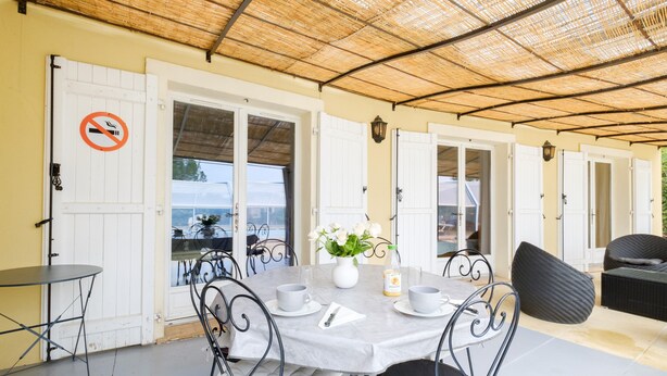 A covered outdoor dining area with a table set for two, surrounded by chairs, and a no-smoking sign on a door. - Holiday Home 'Maison Piscine Chauffe Jacuzzi' with Private Terrace, Private Garden and Wi-Fi (Tourrettes)