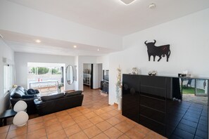 A modern living room with a black sofa, a dining area with a table and chairs, a kitchen with a black cabinet, and a bull-shaped wall decoration.
