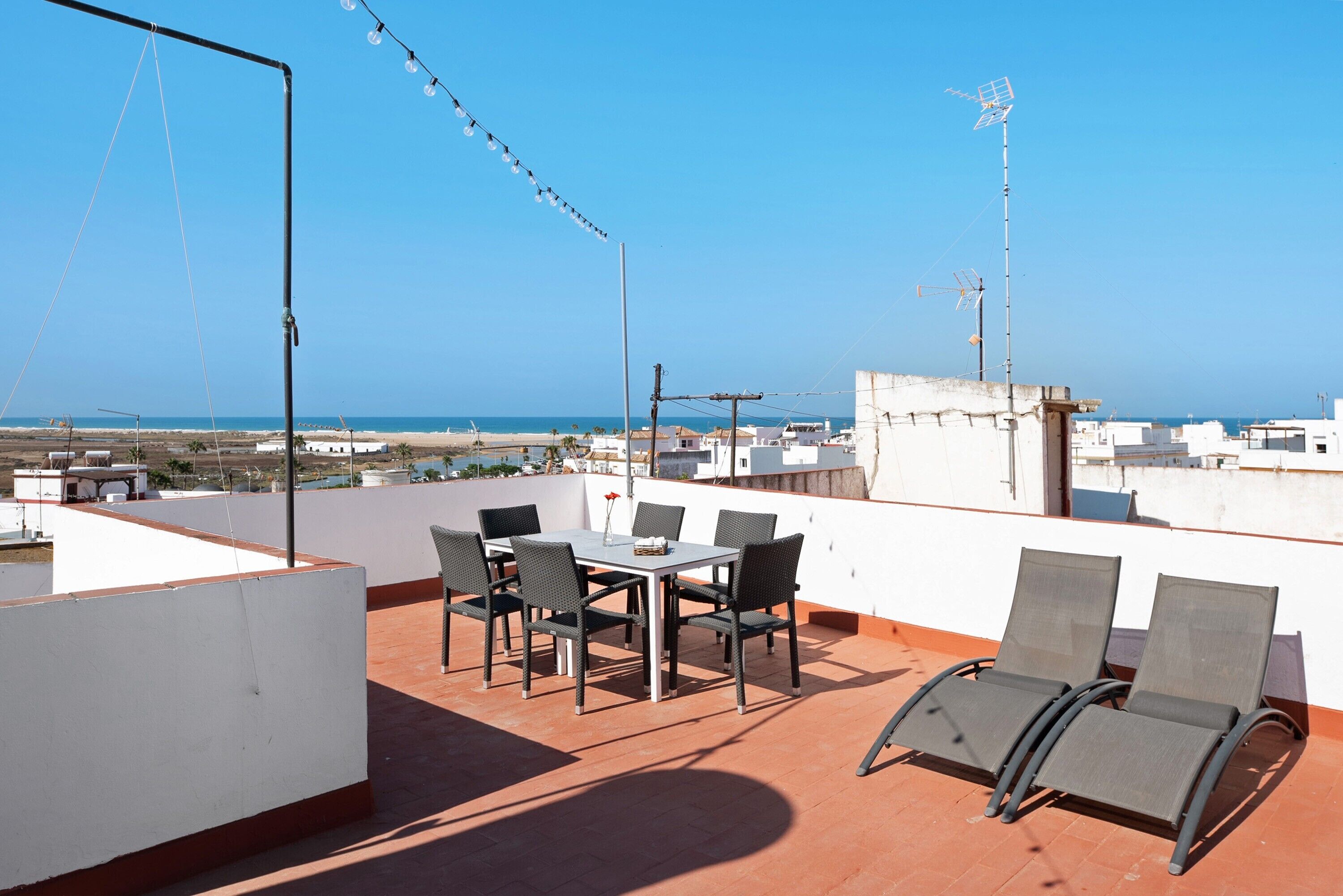 Eine Dachterrasse mit Tisch und Stühlen, mit Blick auf die Küste.