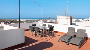 Een terras op het dak met een tafel en stoelen, met uitzicht op de kust.