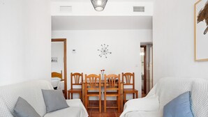 Een kamer met twee bedden, een eettafel met stoelen, een wandklok en een spiegel.