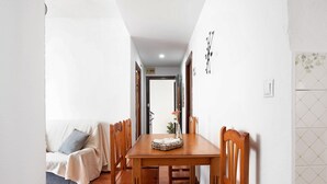 Een eetgedeelte met een houten tafel en stoelen, een bank met plaid, en een betegelde muur met een bloemendesign.